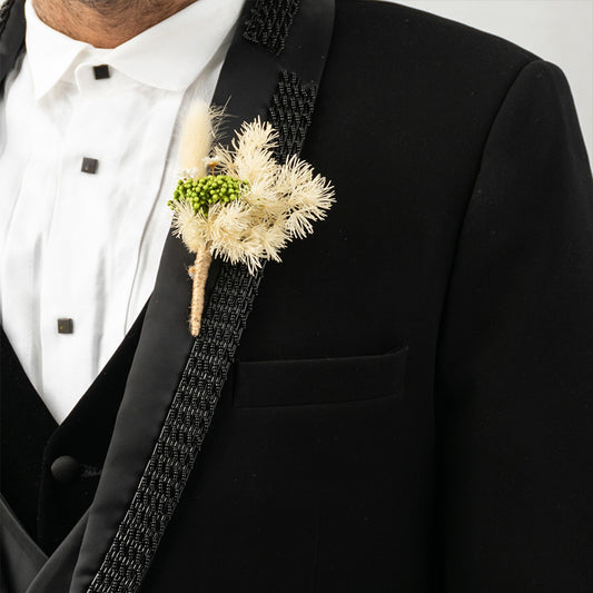 Detailed close up view of an artisanal orange fabric flower boutonniere pinned to a luxury black suit jacket lapel panel.