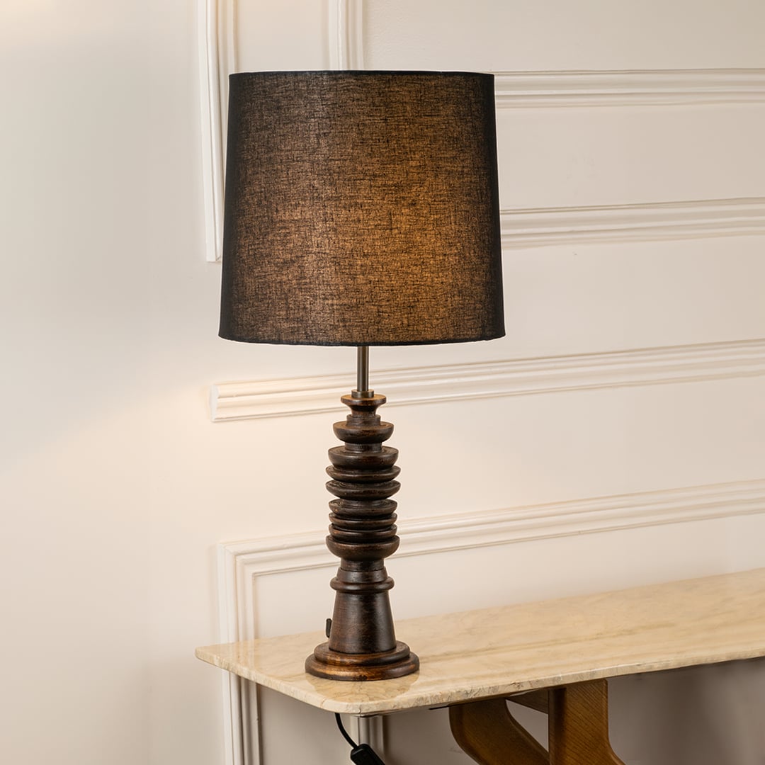 Black fabric shade table lamp with turned wood base casting warm ambient light for elegant bedside table decor.