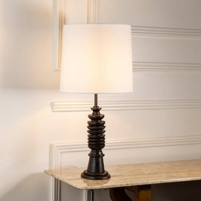 White fabric shade table lamp with turned wood base casting warm ambient light for cozy bedroom and lounge spaces.