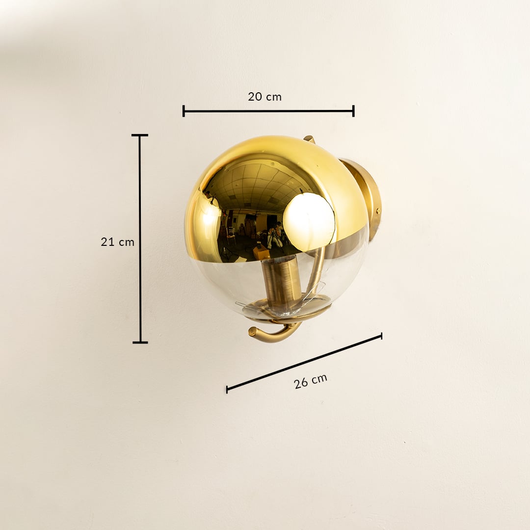 A glass and gold metal wall light measuring 21 cm height 20 cm width and 26 cm depth displayed on a soft white wall creating modern elegant décor.