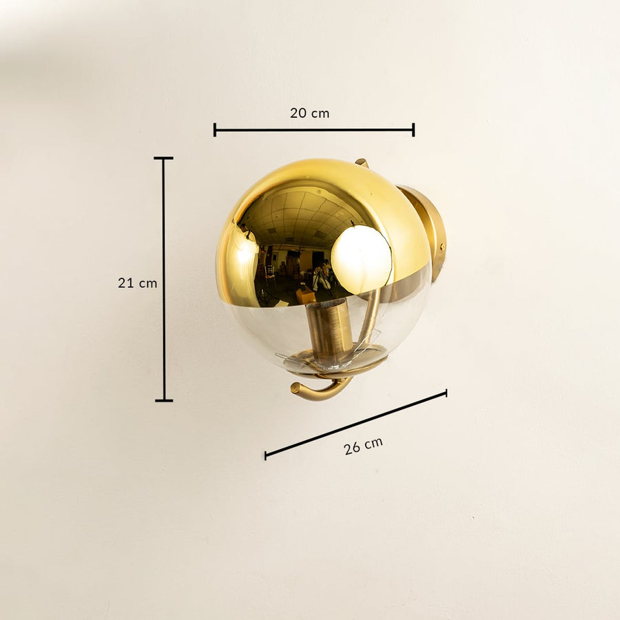 A glass and gold metal wall light measuring 21 cm height 20 cm width and 26 cm depth displayed on a soft white wall creating modern elegant décor.