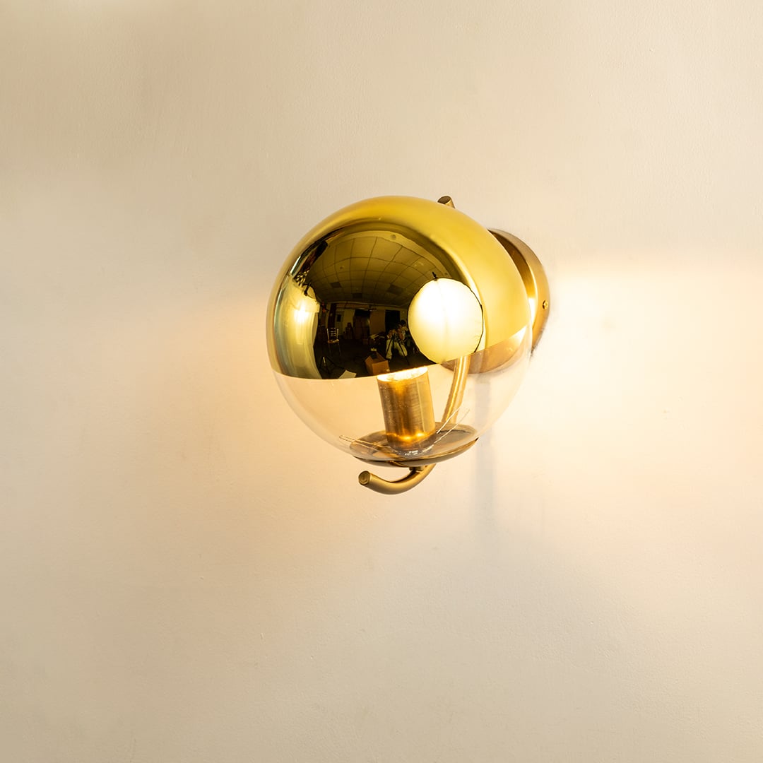 A gold metal and glass wall light shining warmly on a smooth white background creating gentle ambient illumination and adding luxurious modern décor.