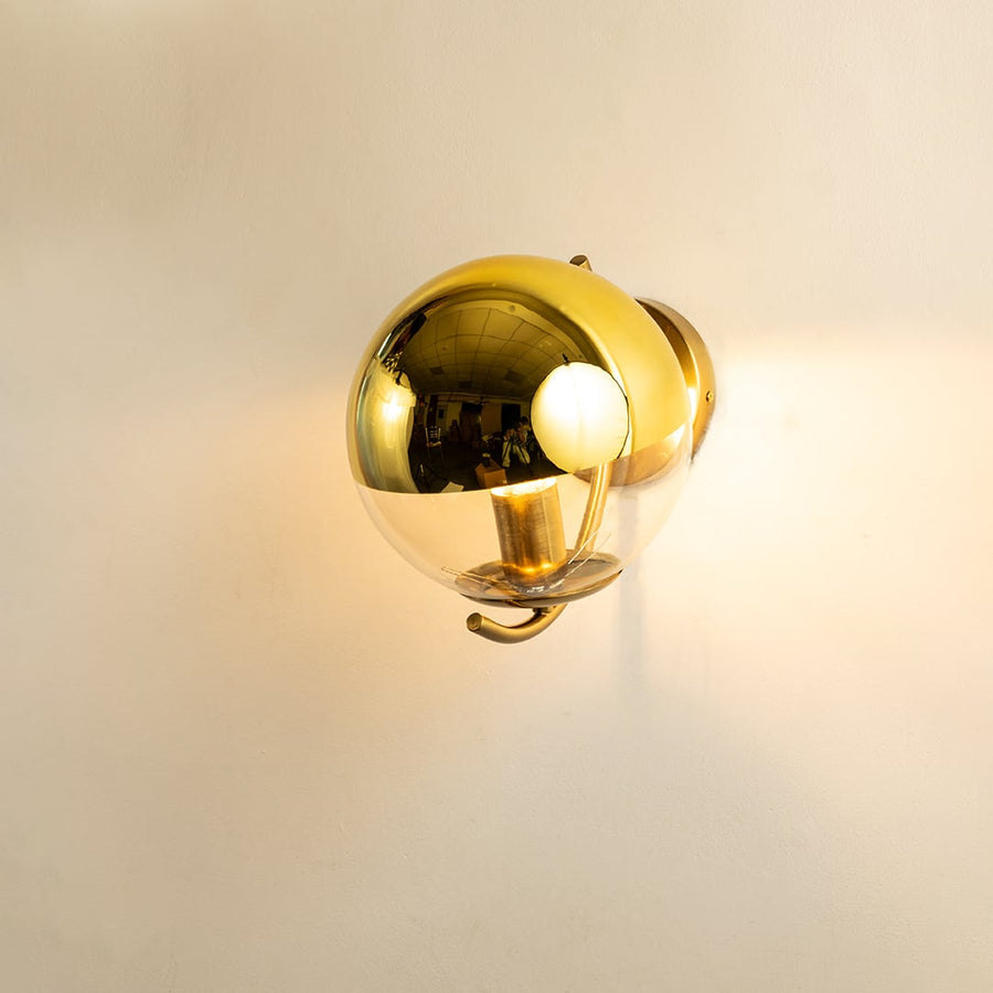 A gold metal and glass wall light shining warmly on a smooth white background creating gentle ambient illumination and adding luxurious modern décor.