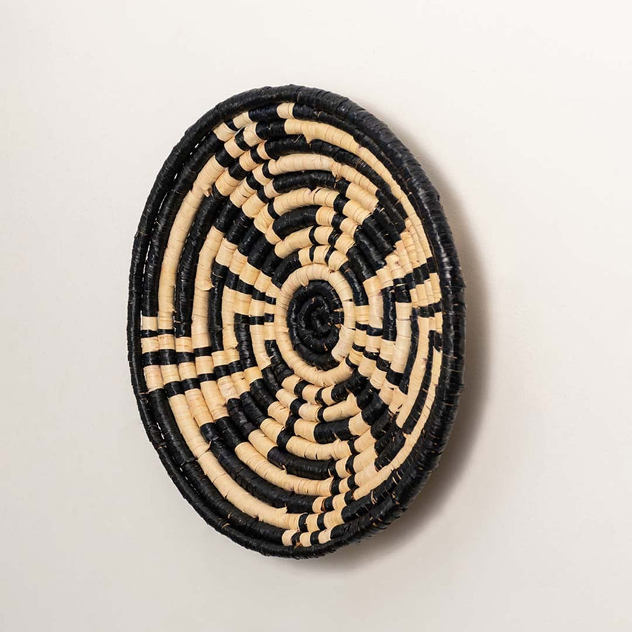 A side angle view of the handwoven black and natural rattan wall basket decor plate showing its raised rim and artisan weave for modern boho home wall styling.