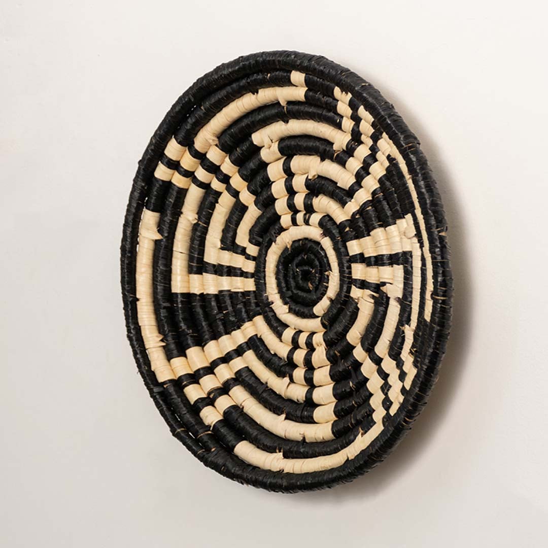 Side profile of the flat woven wall basket showing the thick natural fiber coils and black wrapping details on a white surface.
