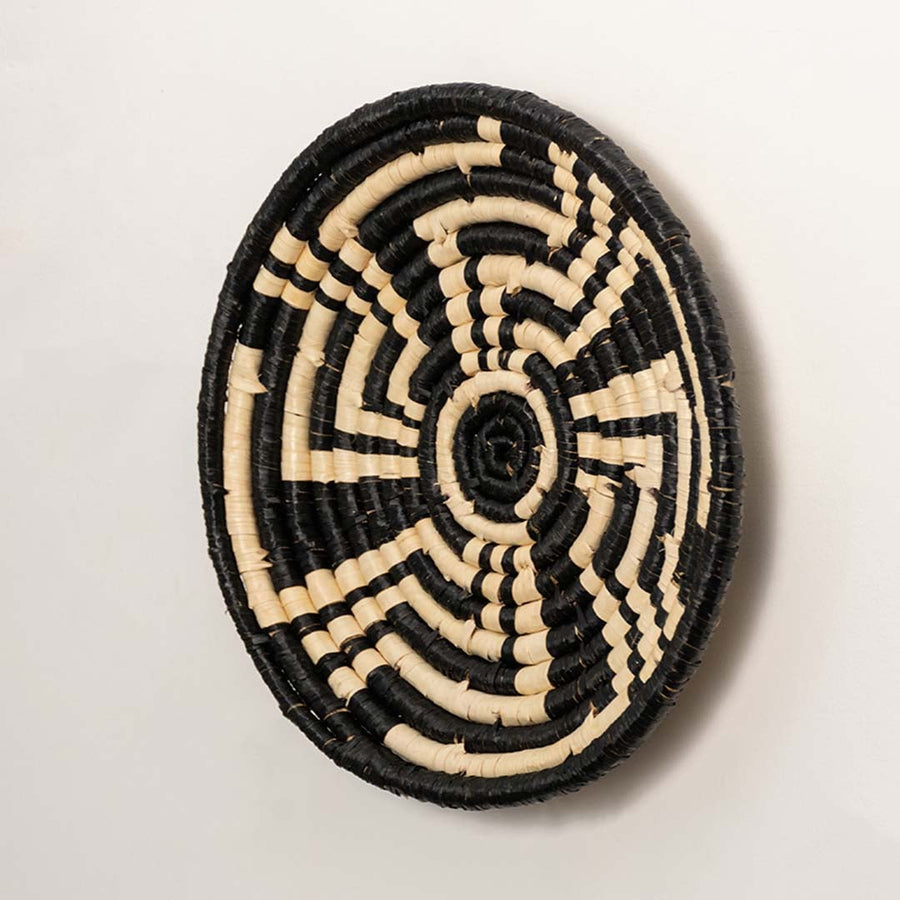 Side profile of the flat woven wall basket showing the thick natural fiber coils and black wrapping details on a white surface.