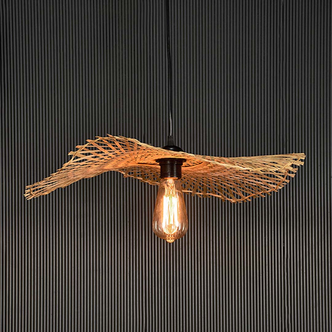 Rattan pendant light with bamboo woven shade and exposed bulb turned on glowing against black background.