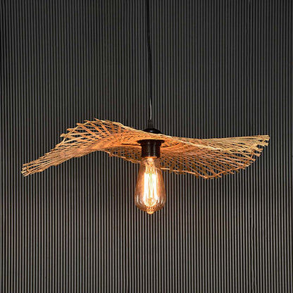 Rattan pendant light with bamboo woven shade and exposed bulb turned on glowing against black background.