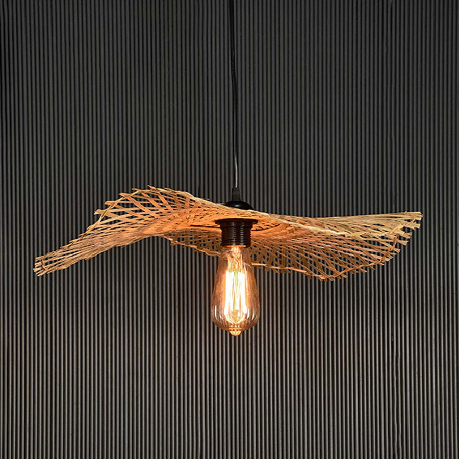Rattan pendant light with bamboo woven shade and exposed bulb turned on glowing against black background.