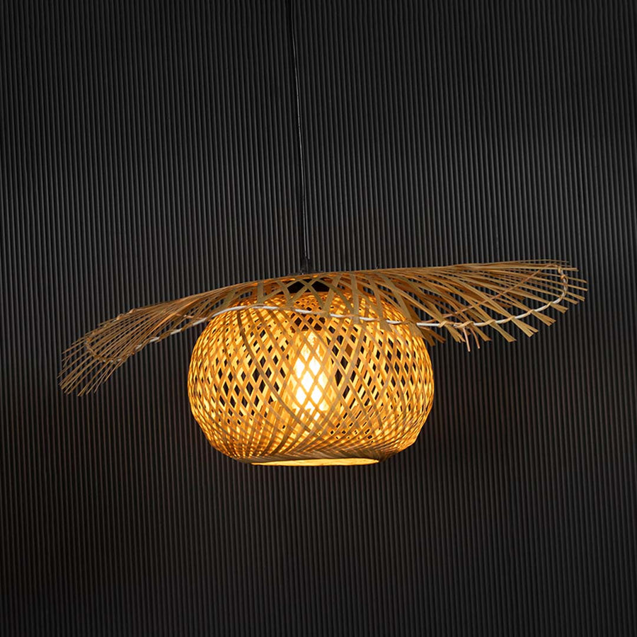 Wide rattan pendant light with handwoven bamboo shade turned on glowing softly against black background