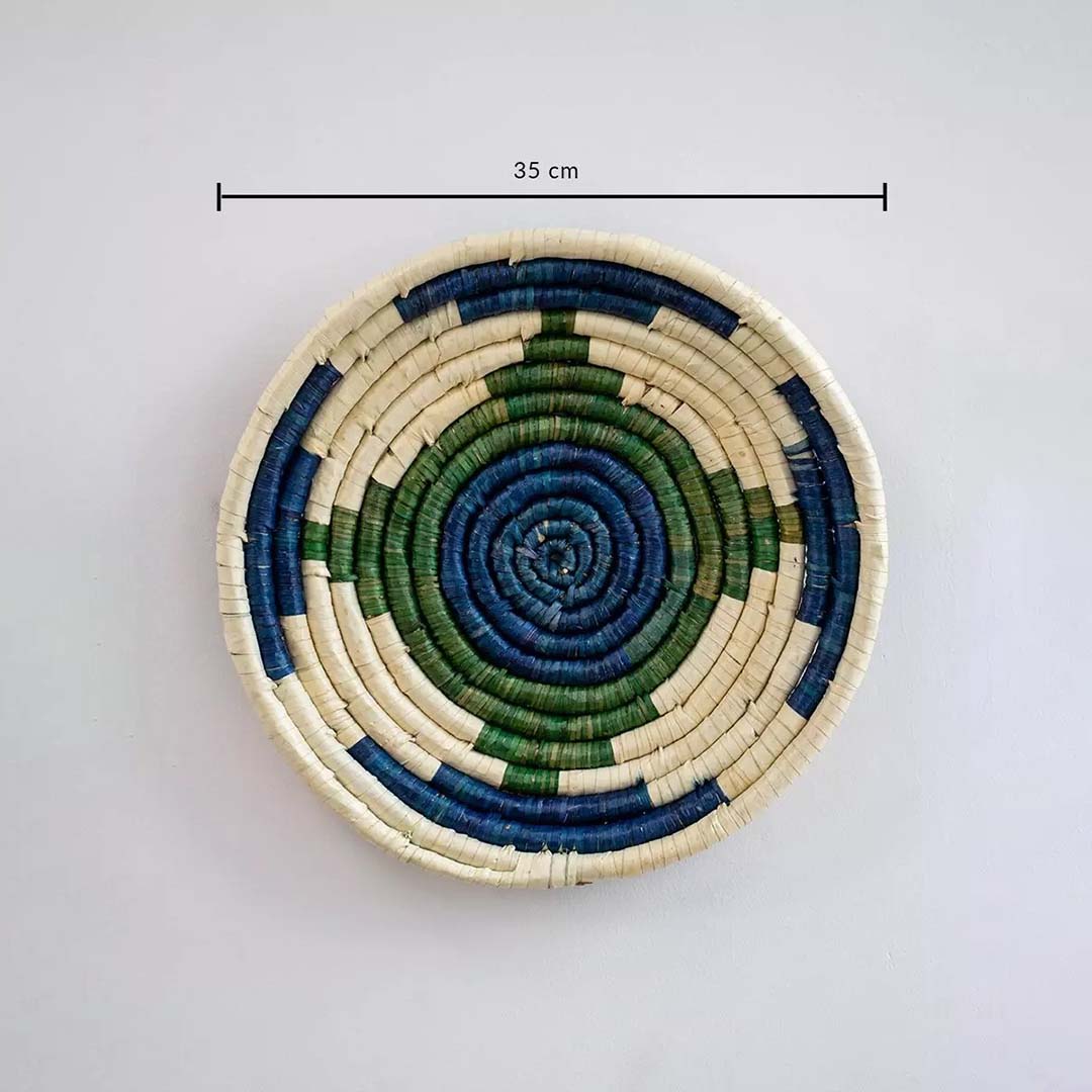 Circular handwoven wall basket in blue green and natural tones showing approx twenty five cm diameter for decorative wall styling.
