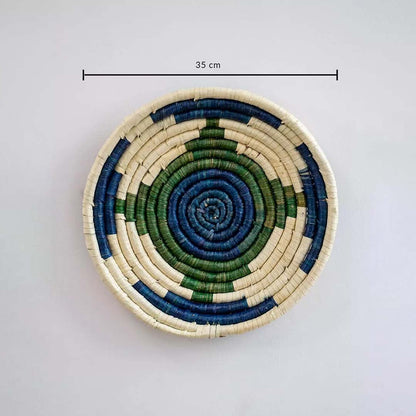 Circular handwoven wall basket in blue green and natural tones showing approx twenty five cm diameter for decorative wall styling.