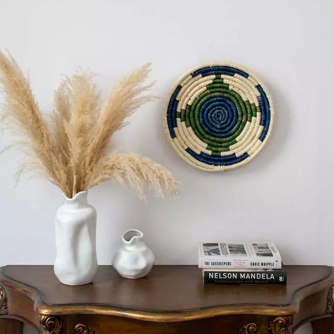 Blue green wall basket styled above a wooden console with ceramic vases and books adding artistic flair to modern interiors.