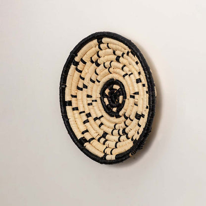 A side angle look at the natural and black rattan wall decor plate showing its raised rim and textured handwoven detailing for warm rustic home wall decor styling.