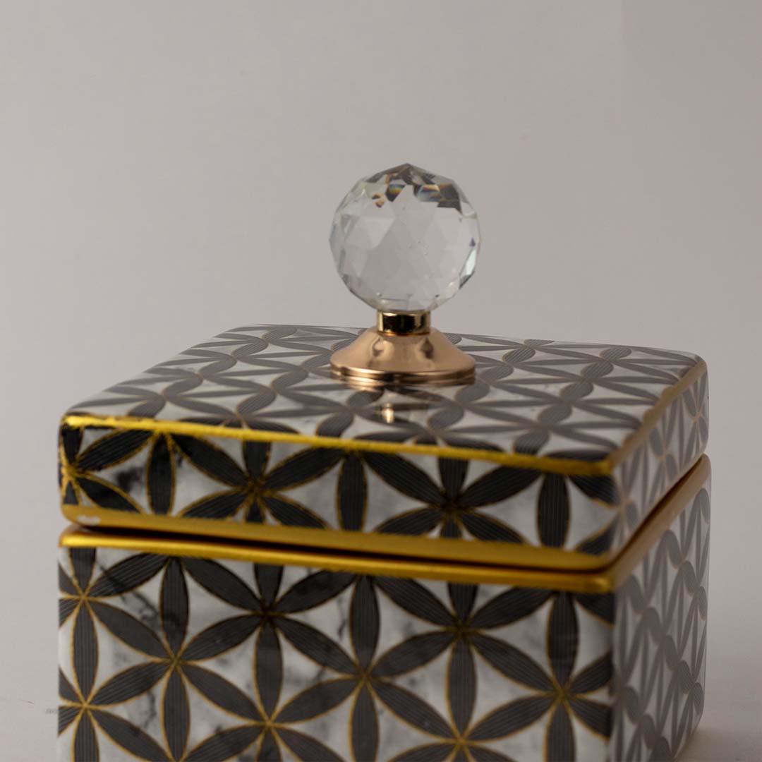 Closeup of black and gold geometric ceramic jar showing detailed flower pattern and elegant crystal lid top.