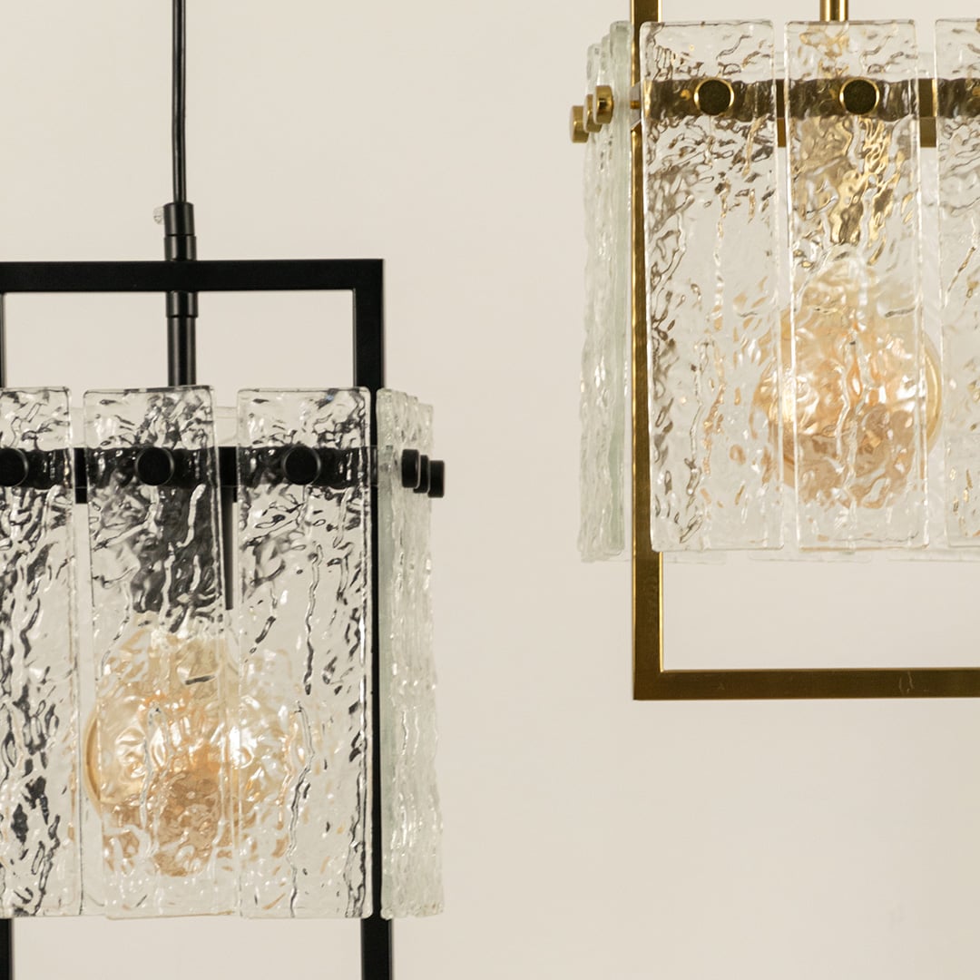 Close view of a pendant light with a textured glass shade and black metal frame showing warm illumination through the detailed glass that adds a refined modern accent to the room.
