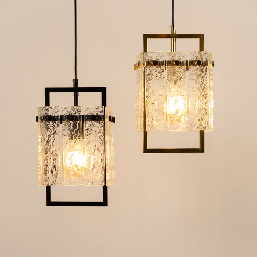 A pair of pendant lights with detailed glass shades and dark frames hanging together and creating a warm patterned glow that adds elegant charm to the interior space.
