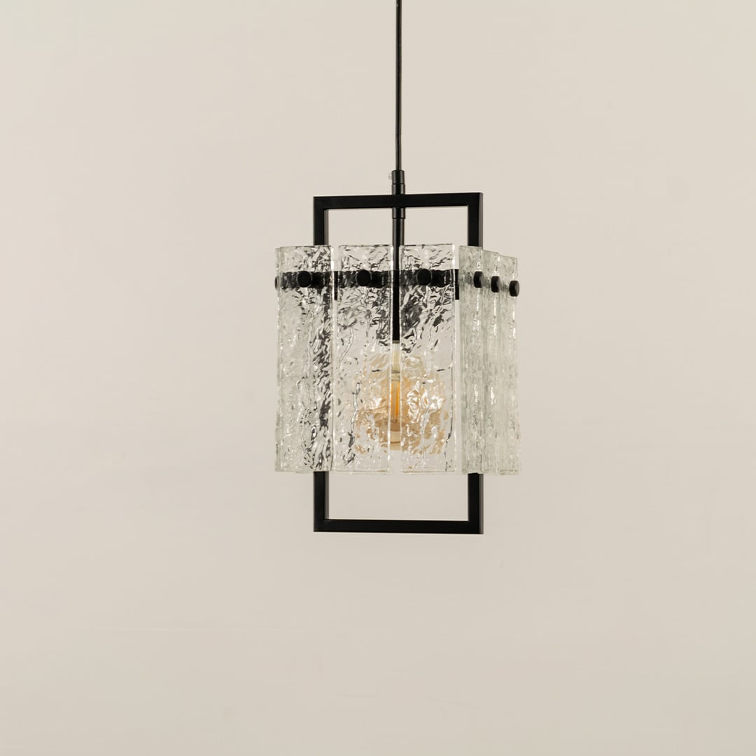 Pendant light with a textured glass shade framed in black metal glowing warmly and creating an elegant patterned illumination that adds a refined modern accent to the interior.