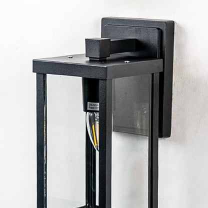 Closeup of outdoor wall light with black frame and transparent glass shade highlighting warm glowing bulb design.