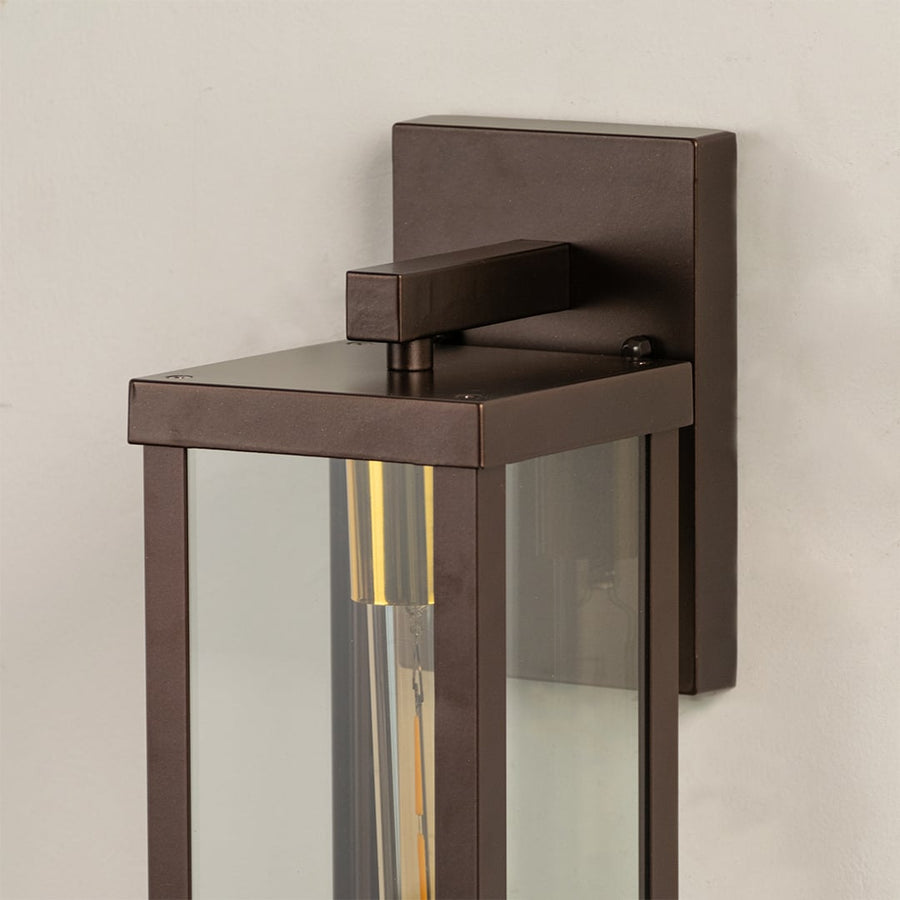 Closeup of bronze metal outdoor wall lantern showing warm tubular bulb inside clear glass frame perfect for modern porch patio and exterior Decor.
