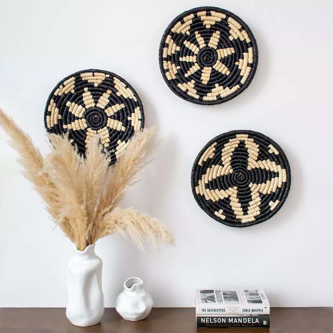 Black handwoven wall basket mounted on a white wall above a wooden console with vases adding a boho touch to home decor.