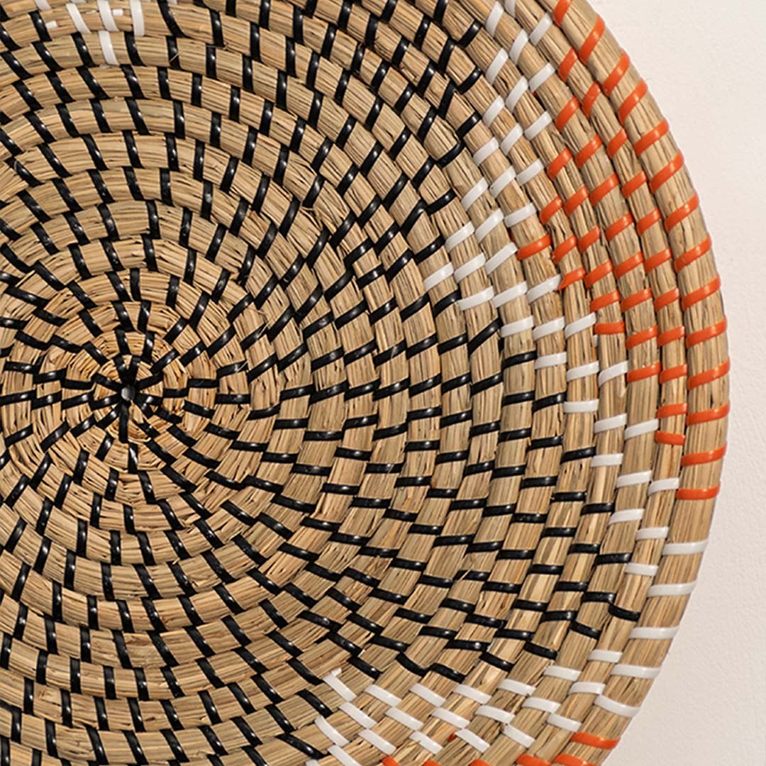 Detailed closeup of woven wall basket pattern with concentric design and warm orange accents showcasing natural material texture.