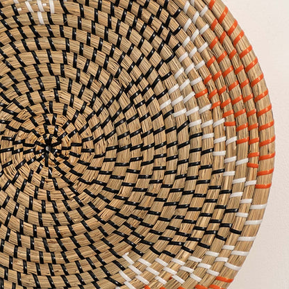 Detailed closeup of woven wall basket pattern with concentric design and warm orange accents showcasing natural material texture.
