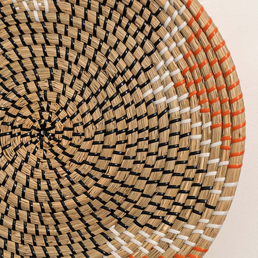 Detailed closeup of woven wall basket pattern with concentric design and warm orange accents showcasing natural material texture.