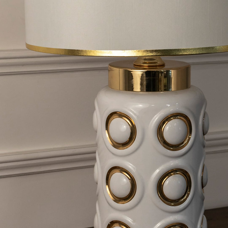 Closeup of white ceramic table lamp featuring circular gold accents and polished detailing with premium modern finish.