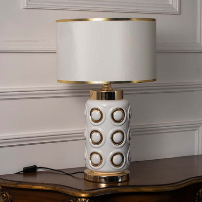 White and gold table lamp with geometric ceramic base and metallic accents shown against a white wall for clean product view.