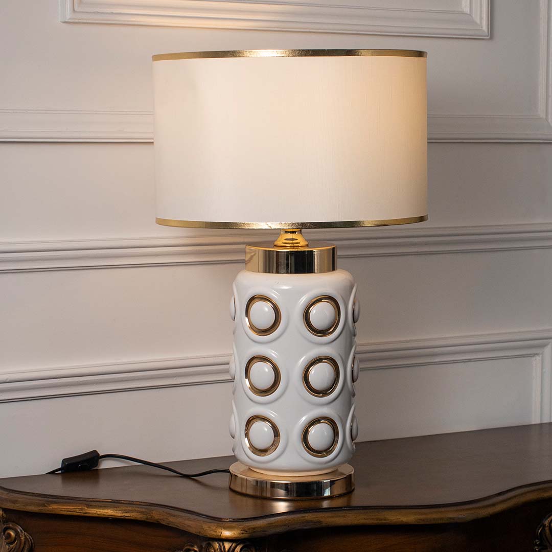 White ceramic table lamp with geometric gold accents and fabric shade for modern luxury interior styling.
