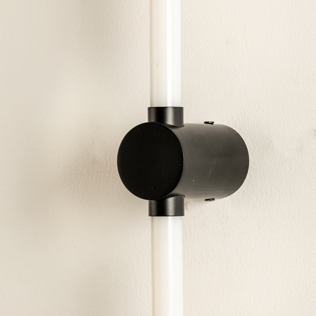 Closeup of wall light with cylindrical black metal mount and glowing tube showcasing sleek modern design for interior decor styling.