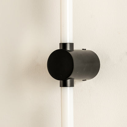 Closeup of wall light with cylindrical black metal mount and glowing tube showcasing sleek modern design for interior decor styling.
