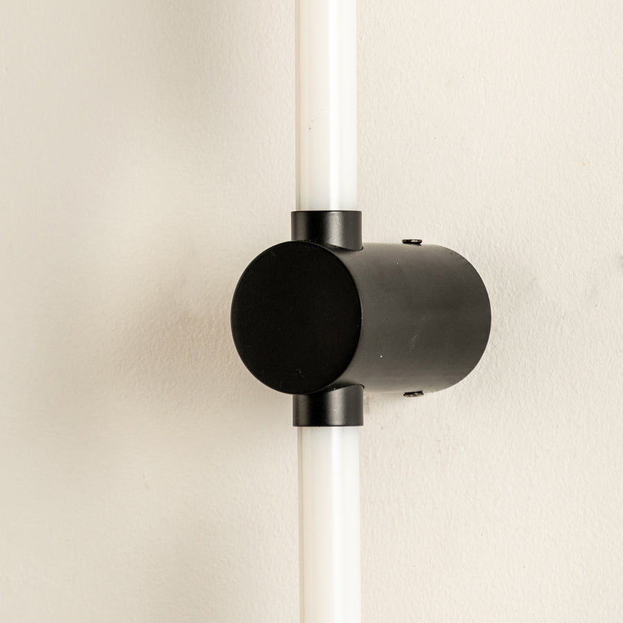 Closeup of wall light with cylindrical black metal mount and glowing tube showcasing sleek modern design for interior decor styling.