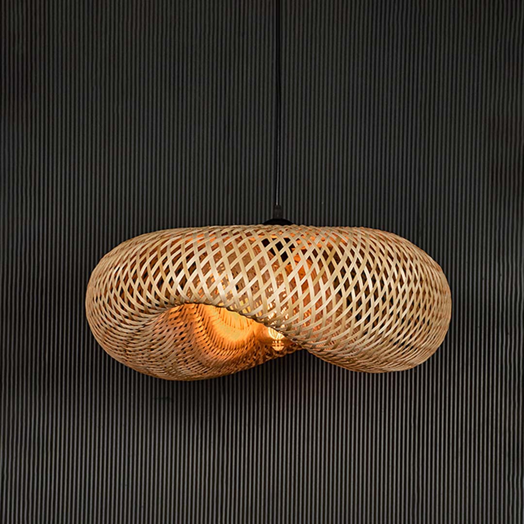 Wide rattan pendant light with woven bamboo shade turned on glowing softly against plain black background.