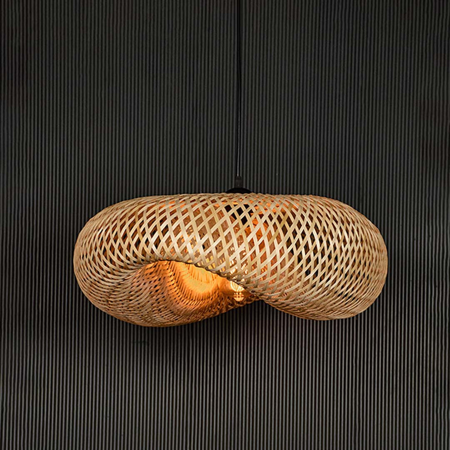 Wide rattan pendant light with woven bamboo shade turned on glowing softly against plain black background.