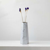 Purple dried globe thistle stems styled in tall marble ceramic vase against white wall elegant lifestyle home decor.