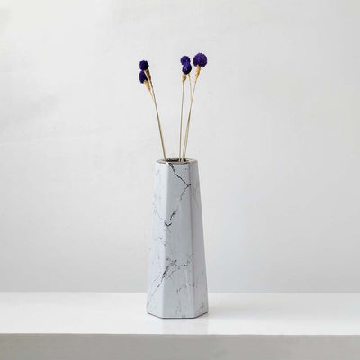 Purple dried globe thistle stems styled in tall marble ceramic vase against white wall elegant lifestyle home decor.
