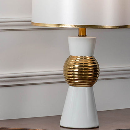 Closeup view of white and gold table lamp with textured golden round base and white shade.