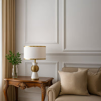 White and gold table lamp with textured round base styled in a modern living room on a wooden side table.