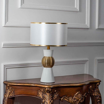 White and gold table lamp with textured golden round base turned off against white background.