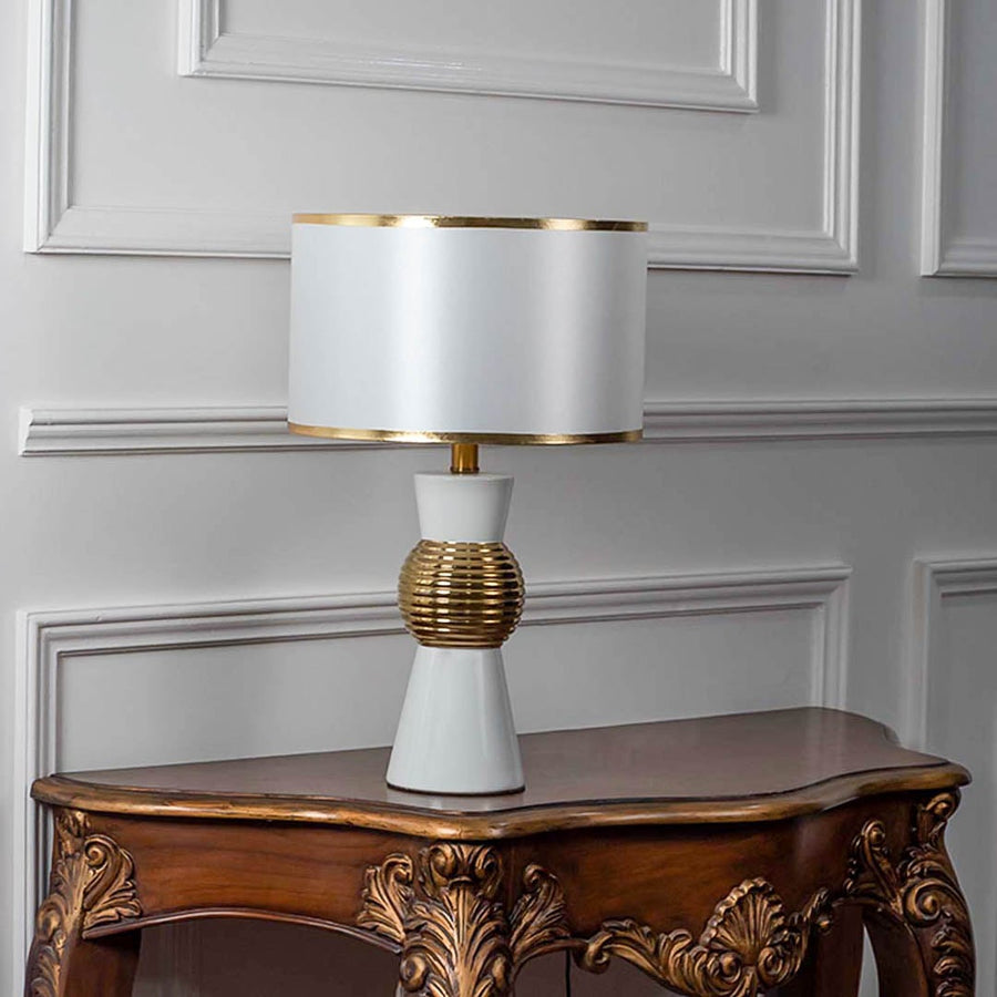 White and gold table lamp with textured golden round base turned off against white background.