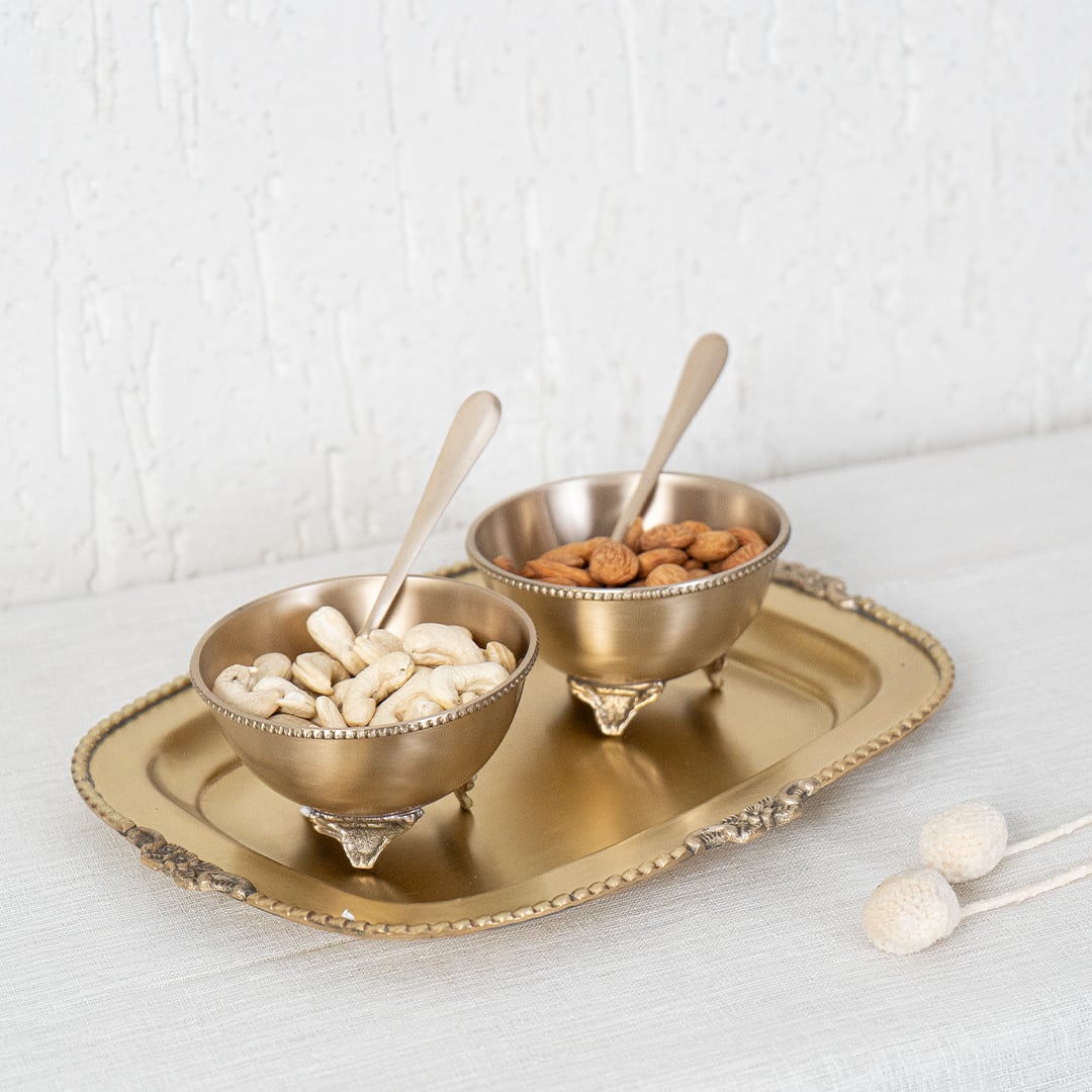 Gold metal condiment bowl set lifestyle image with snacks on decorative tray for luxury dining table decor.