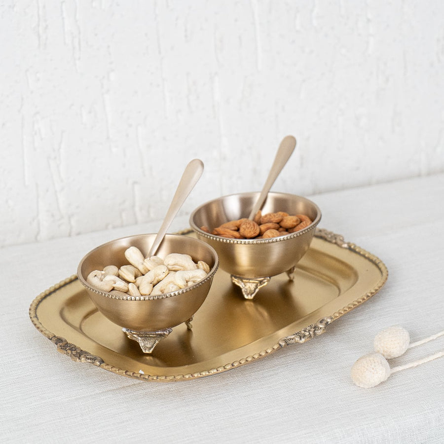 Gold metal condiment bowl set lifestyle image with snacks on decorative tray for luxury dining table decor.