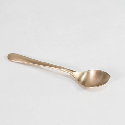 Single matte gold spoon with smooth curved handle and round bowl head shown on plain white background.
