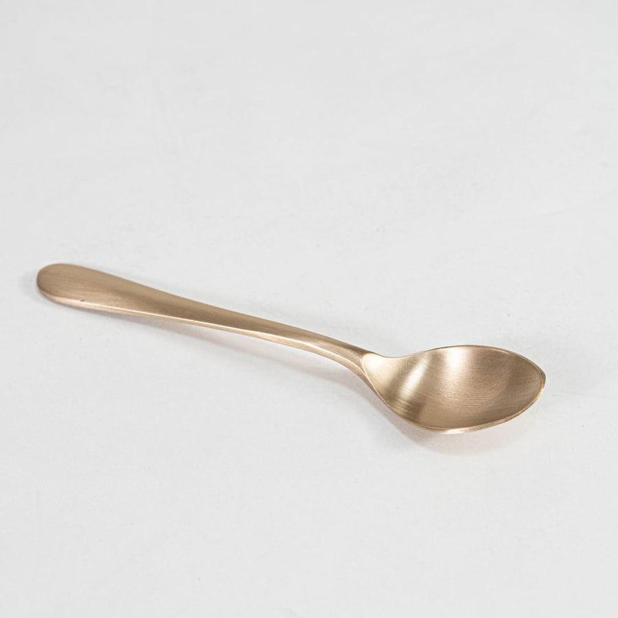 Single matte gold spoon with smooth curved handle and round bowl head shown on plain white background.