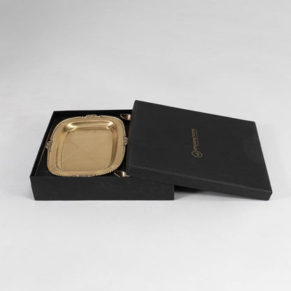Elegant gold tray and bowl set partially packed in black luxury box with branded lid placed on white backdrop.
