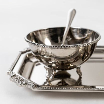 Elegant silver tray set with bowls and spoons partially shown inside open black gift box with gold branding.