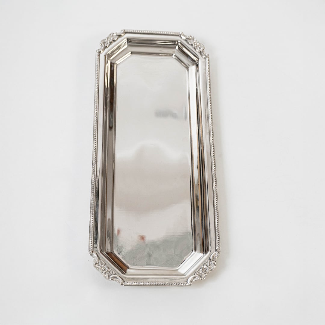 Long rectangular silver tray displayed on a white background showing its reflective finish ornate edging and elegant elongated structure.