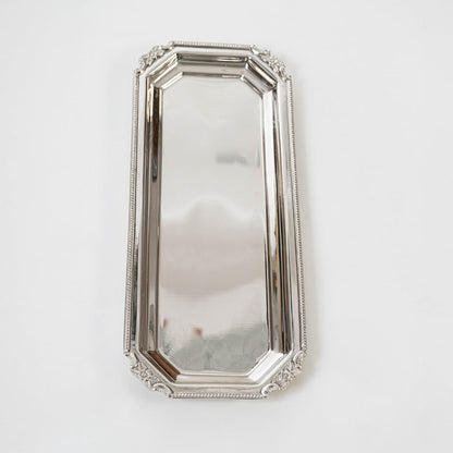 Long rectangular silver tray displayed on a white background showing its reflective finish ornate edging and elegant elongated structure.